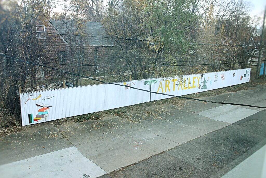 Jerjuan Howard: Community Enhancement Through Literacy Image 7 Looking down across the street from a white-painted picket fence reading "Puritan Ave ART ALLEY".