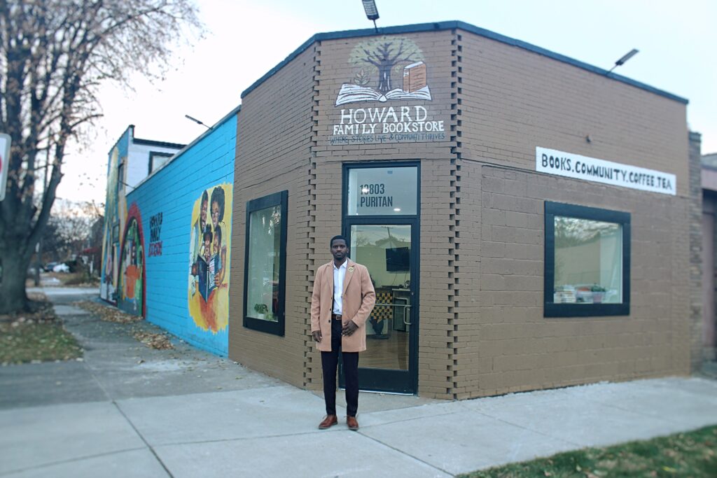 Jerjuan Howard: Community Enhancement Through Literacy Image 2 Jerjuan Howard, a dapper young black man, standing in front of a small corner store. "Howard Family Bookstore" is painted above the door, and "Books. Community. Coffee. Tea." painted above the side window.