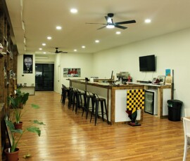 Cafe space at Howard Family Bookstore in Detroit. Photo ©2025 by Ryan M Place. All rights reserved. Stark white room featuring a rustic wooden cafe counter, metal stools, and a large screen TV/Menu board.