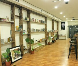 Interior bookshelves and cafe space at Howard Family Bookstore in Detroit. Photo ©2025 by Ryan M Place. All rights reserved. Sparcely spaced rustic wooden shelves on a white wall, featuring several books. Cafe counter with metal stools.