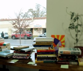 Howard Family Bookstore (Interior) in Detroit. Photo ©2025 by Ryan M Place. All rights reserved. Stacks of books on a table in front of a window.