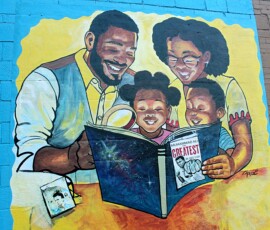 Mural on the exterior wall of Howard Family Bookstore in Detroit. Photo ©2025 by Ryan M Place. All rights reserved. Mural on brick wall featuring a black family (father, mother, daughter, son) reading a book about Muhammad Ali.