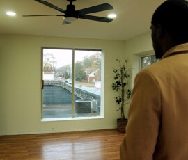 Upstairs space above Howard Family Bookstore in Detroit. Photo ©2025 by Ryan M Place. All rights reserved. Over back shoulder photo of a man standing in a nearly-vacant white room with a barn door, artificial plant, and window overlooking a roof.