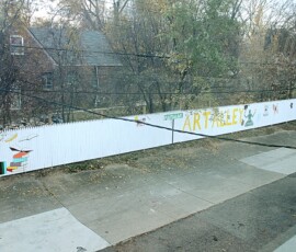Puritan Avenue Art Alley. Photo ©2025 by Ryan M Place. All rights reserved. Looking down across the street from a white-painted picket fence reading "Puritan Ave ART ALLEY".