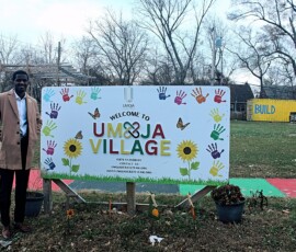 Umoja Community Garden sign in Detroit. Photo ©2025 by Ryan M Place. All rights reserved. Handsome black man standing next to a sign in front of a field.