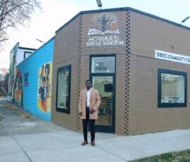 Jerjuan Howard in front of Howard Family Bookstore in Detroit. Photo ©2025 by Ryan M Place. All rights reserved. Jerjuan Howard, a dapper young black man, standing in front of a small corner store. "Howard Family Bookstore" is painted above the door, and "Books. Community. Coffee. Tea." painted above the side window.